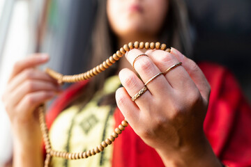 Muslim woman in headscarf and hijab prays with her hands up in air while holding rosary in...