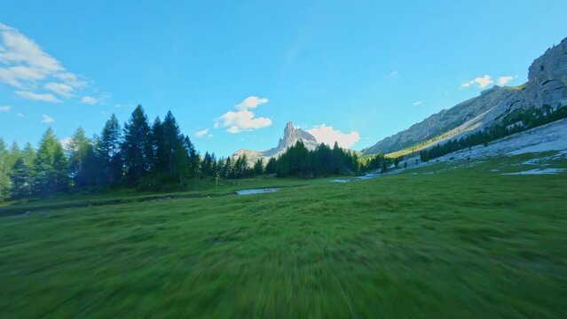 fpv drone flying over alpine pasture and forest with mountain peak in the backgroud at Lago do crado Dolomites Italy