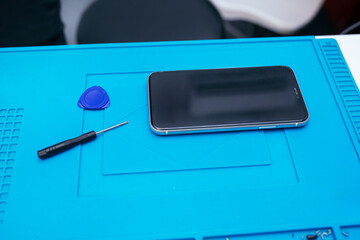 Smartphone on blue mat with repair tools nearby.