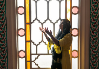 Muslim woman in headscarf praying with her hands open in the mosque