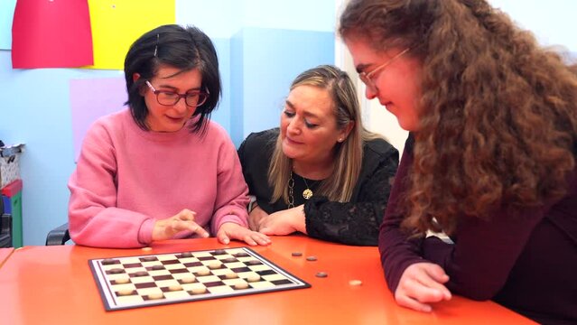 Caregiver and woman with special needs playing with board games on a table of a day center