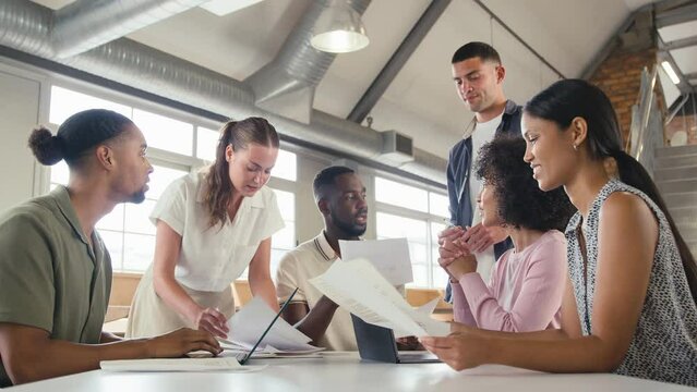 Smiling multi-cultural business team meeting around table in modern open plan office discussing document and collaborating together - shot in slow motion