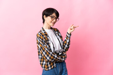 Young photographer woman isolated on pink background pointing finger to the side