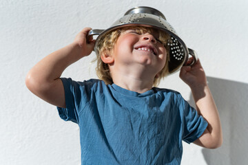 Little boy putting colander on his head . cheerful blond boy with a sieve on his head. positive kid