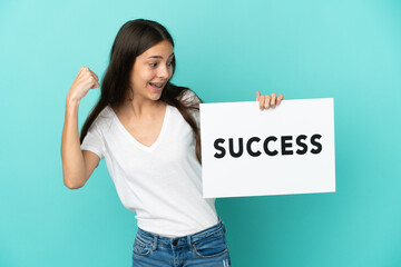 Young French woman isolated on blue background holding a placard with text SUCCESS and celebrating a victory