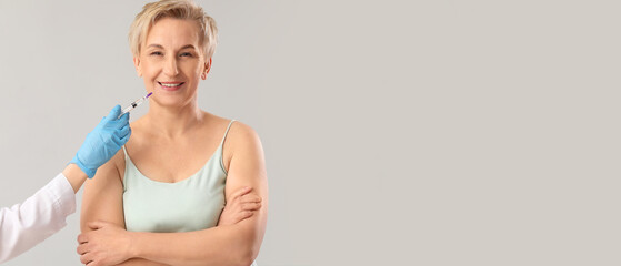 Mature woman receiving filler injection on grey background with space for text