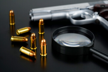 Ammunition and magnifying glass put on a black desk with blurred short pistol background, pistol, ammo and magnifying glass represents related to the concept murder cases of weapons detective.