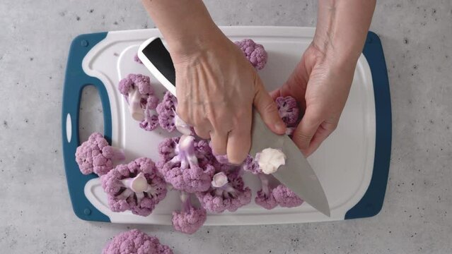 Woman devided purple cauliflower into florets, the cooking process, view from above. 