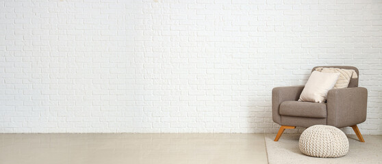 Cozy grey armchair with cushions and pouf near white brick wall. Banner for design