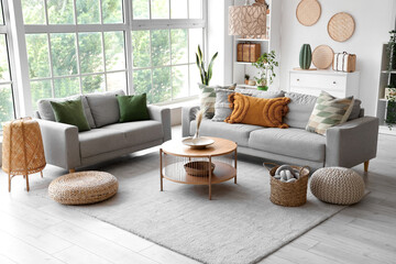 Interior of light living room with grey sofas, coffee table and wicker poufs