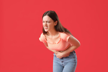 Young woman suffering from stomach ache on red background - obrazy, fototapety, plakaty