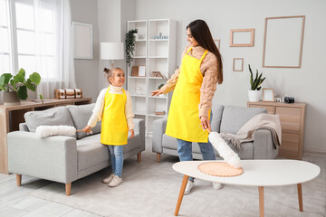 Happy mother and her little daughter with pp-dusters cleaning living room together