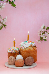 Two paski with burning candles and eggs on pink background
