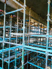 A construction site with scaffolding and a lot of blue and green metal. Scene is industrial and possibly chaotic