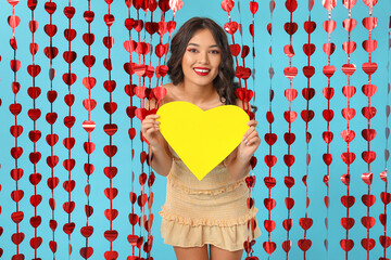 Beautiful young Asian woman with paper heart and garland on blue background. Valentine's Day...