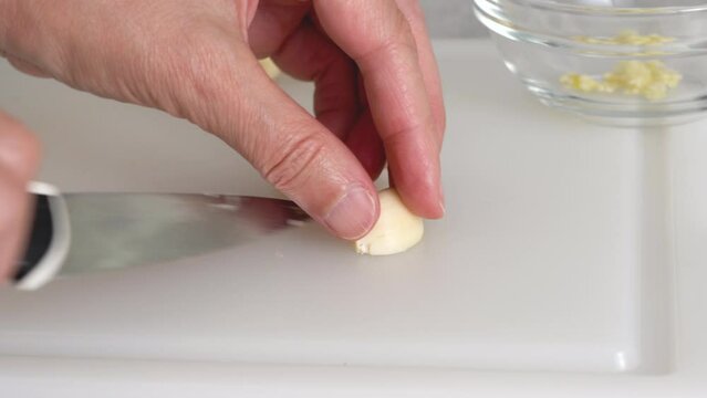 The chef chopping garlic on a white plastic cutting board, close-up view, preparation process