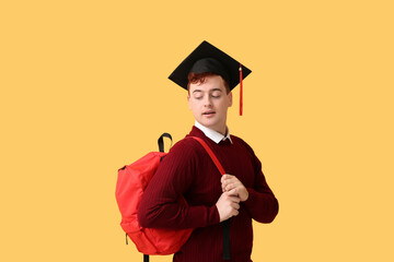 Male student in mortar board with backpack on yellow background