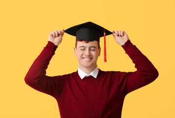 Happy male student in mortar board on yellow background