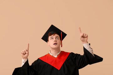 Male graduating student pointing at something on beige background