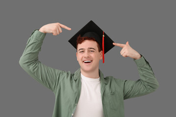 Male student pointing at mortar board on grey background