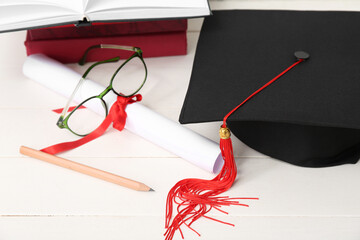 Mortar board with diploma, eyeglasses and notebooks on white wooden background