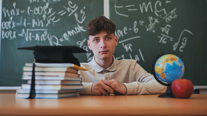 Portrait of a high school student against a background of blackboard, globe and books with cap.