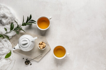 Cups of tea, teapot and spoon with dry leaves on light background