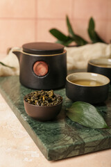 Cup of tea, teapot and bowl with dry leaves on light background