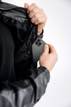 A close-up photo on a white background of a man taking out a gadget from the inside pocket of his jacket. The guy is holding a gadget in his inner pocket