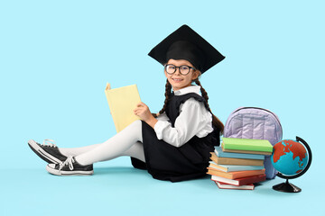 Little girl in graduation hat reading book on blue background. End of school year