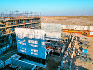 A construction site with scaffolding and a large building in the background. The sky is clear and blue