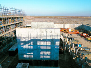 A construction site with scaffolding and a large building in the background. The sky is clear and blue