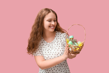 Beautiful young happy woman with wicker basket full of decorative cosmetics on pink background