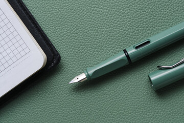 Fountain pen and notebook green leather background.