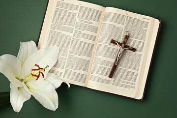 A symbolic Christian composition with Holy Bible lies beside a fresh white lily on a dark...
