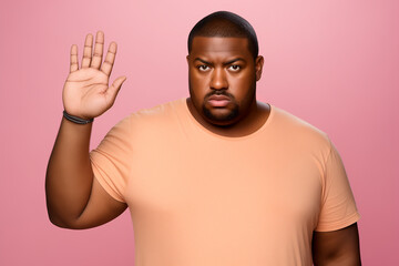Serious displeased african american overweight man wearing basic casual orange t-shirt standing showing stop gesture with palm looking camera isolated on pastel pink background studio portrait