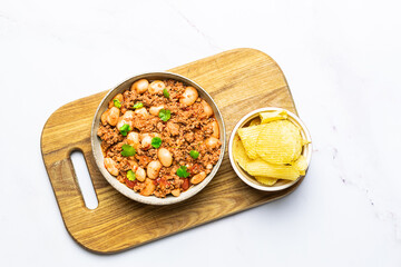Tasty homemade chili con carne with chips on the wooden tray on white marble table top view.