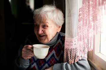 An elderly woman laughs and drinks tea at the table.