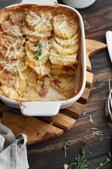 Potato gratin with bacon, thyme and cheese on wooden background