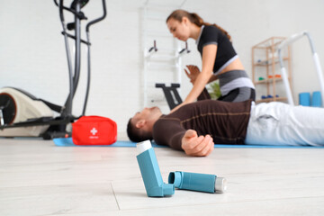 Asthma inhalers and trainer giving man first aid in gym, closeup - obrazy, fototapety, plakaty