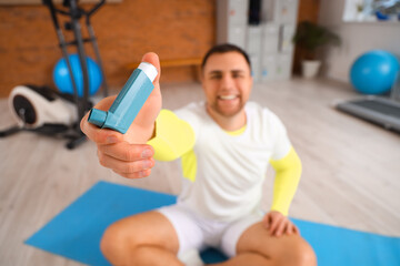 Sporty young man with inhaler sitting in gym, closeup