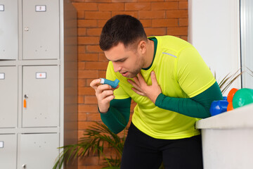 Sporty young man with asthma attack using inhaler in gym
