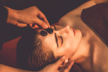 Caucasian woman enjoying relaxing anti-stress head massage with hot stone and pampering facial...