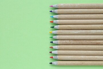 Obraz premium Multi colored pencils isolated on green background. Back to school concept. Sketching and drawing hobby. Stationery supply store. Education process. Top view. Minimal style composition