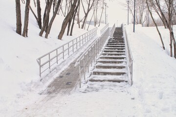 Stairs and ramp with metal railings for the passage of strollers and wheelchairs in public park at winter time. Comfortable barrier-free urban environment in city. Pathway for people with disabilities