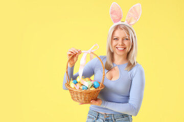 Beautiful woman in bunny ears with Easter eggs on yellow background