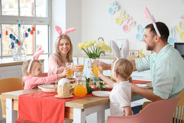Happy family in bunny ears with juice having Easter dinner at home