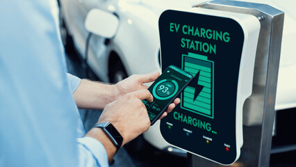 Businessman holding smartphone display battery status interface by smart EV mobile application...