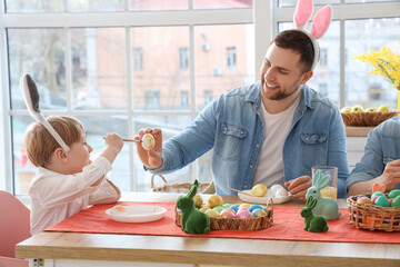 Cute little boy with his father painting Easter egg at home
