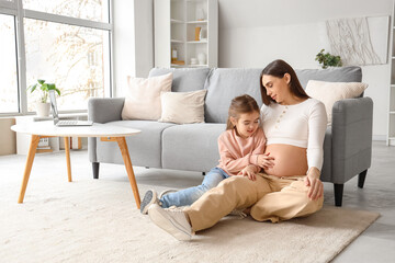 Young pregnant woman with her little daughter touching belly at home